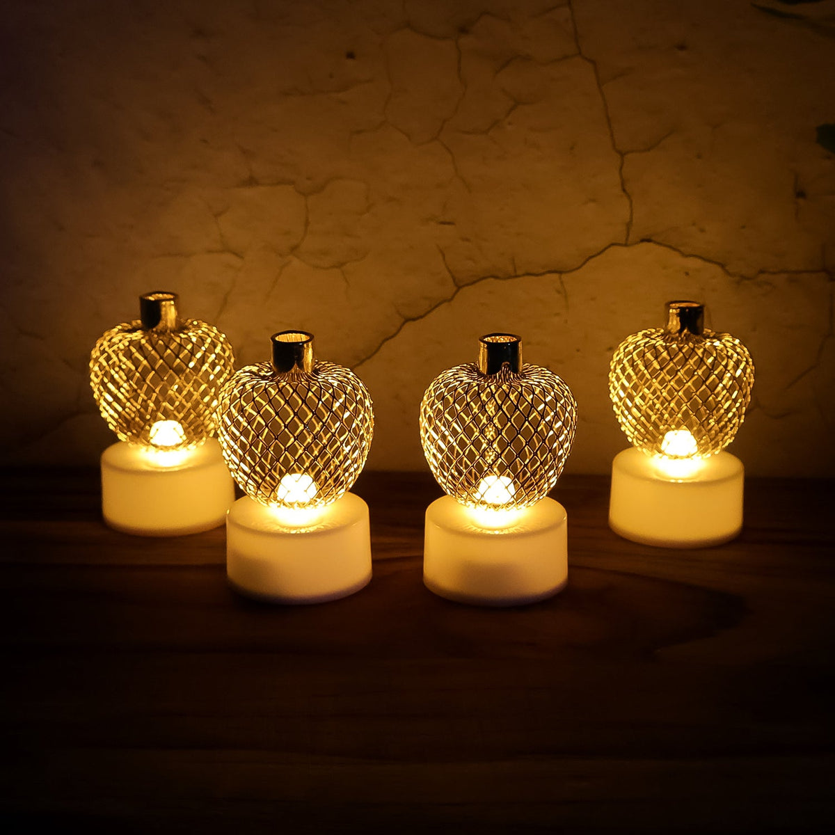 Set of four golden apple LED tealight candles glowing warmly. Main image