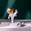 Astronaut Phone Holder (kicking leg design) on a wooden desk, holding a smartphone.