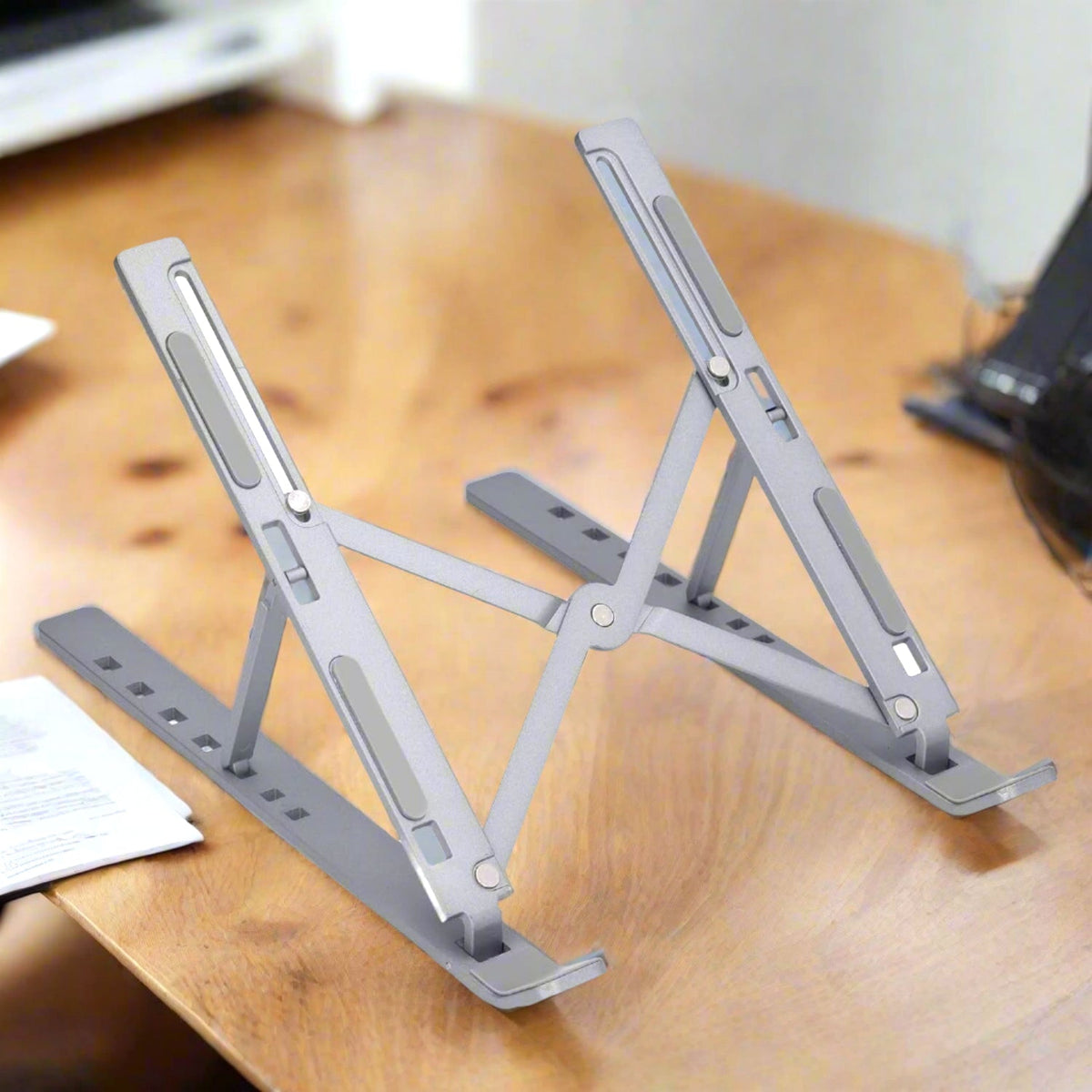 A person uses a silver metal portable laptop stand with a laptop on a desk. Main image