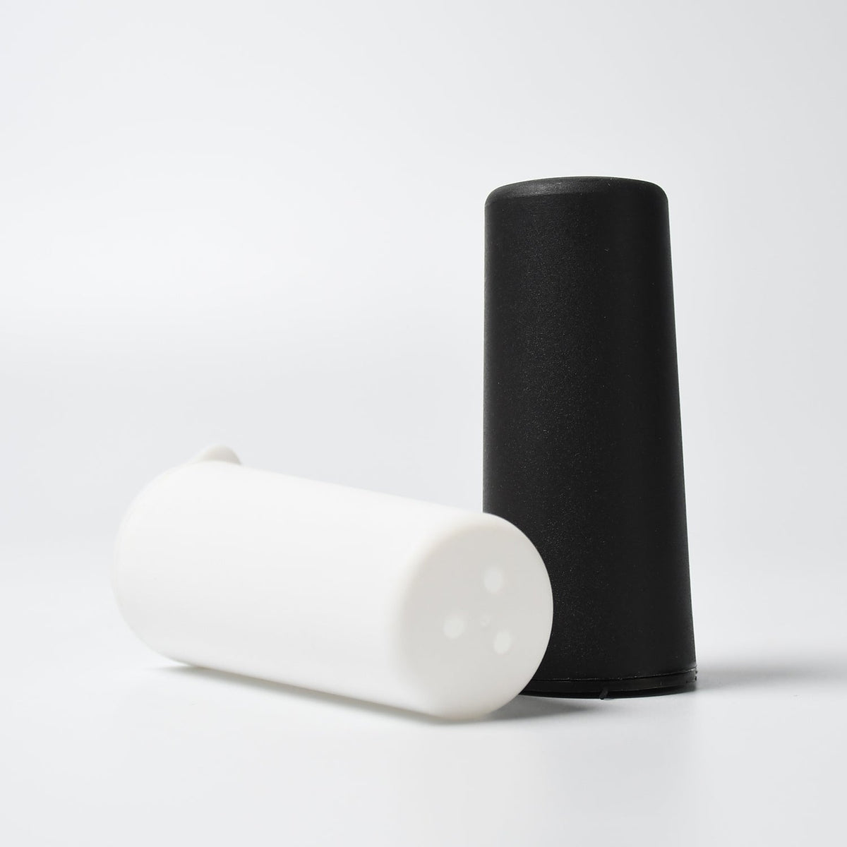 Polycarbonate spice dispensers pouring salt and pepper onto a dish. Main image