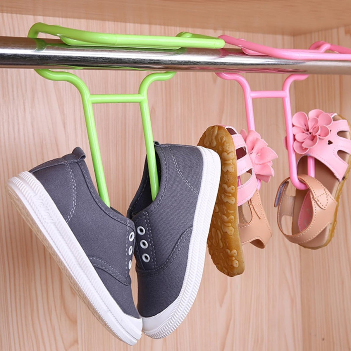 A pair of grey canvas shoes and pink sandals hang from green and pink plastic Organivo shoe drying racks on a metal rod. Main image