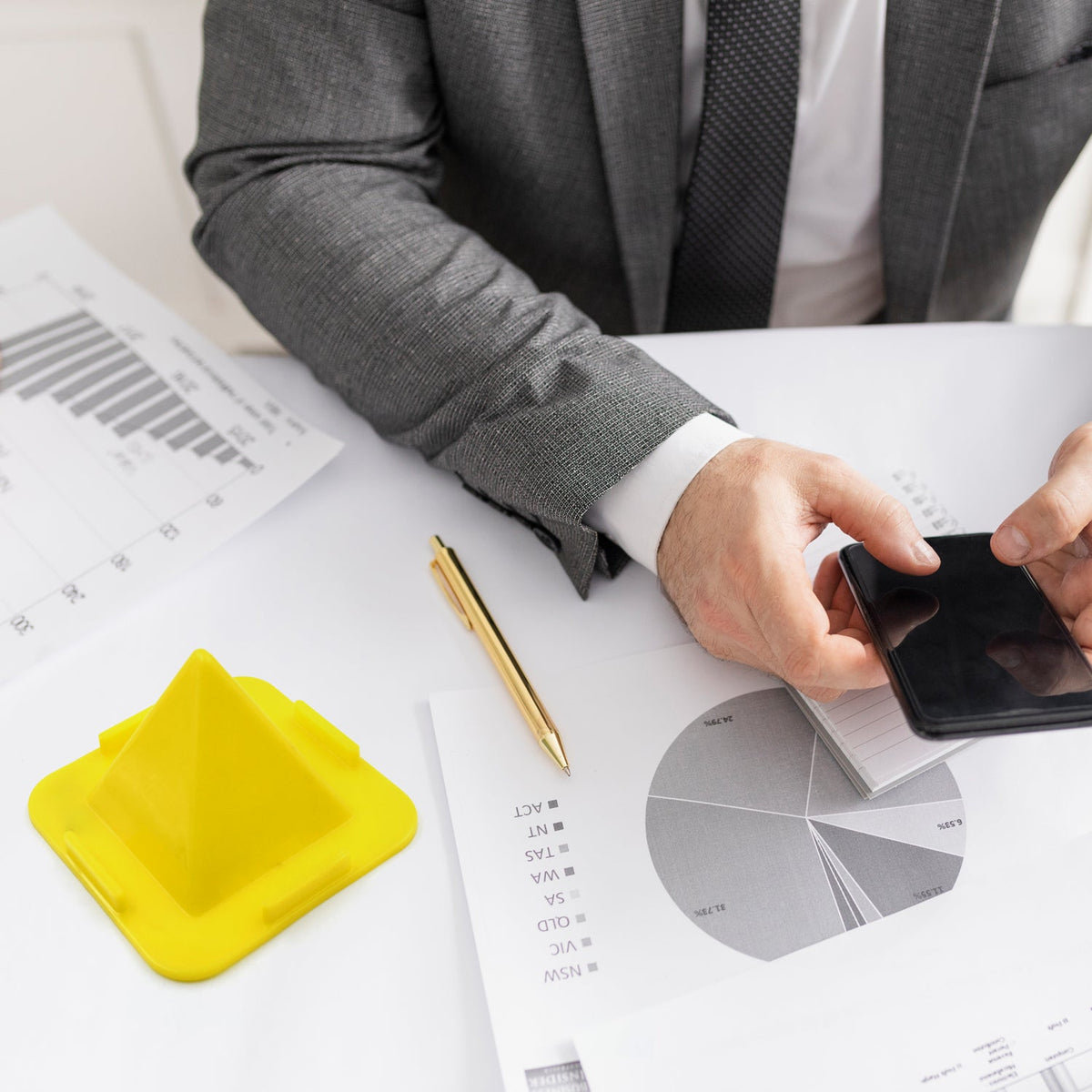 A flexible pyramid mobile stand in black, holding a smartphone upright on a desk. Main image