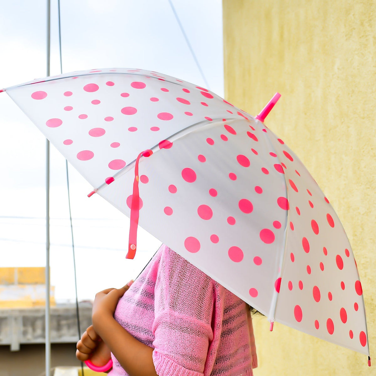 A person holds a white umbrella with bright pink polka dots, featuring a matching pink handle and tip. Main image