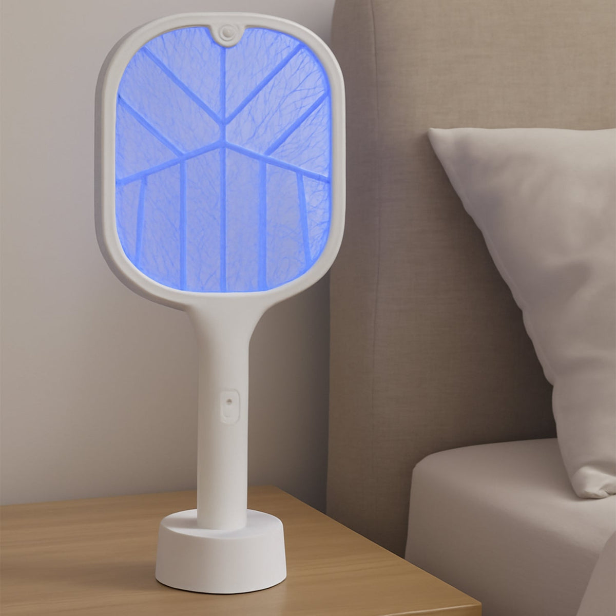 A white FlyTamer mosquito killer racket with a glowing blue UV light stands on a wooden nightstand next to a bed. Main image
