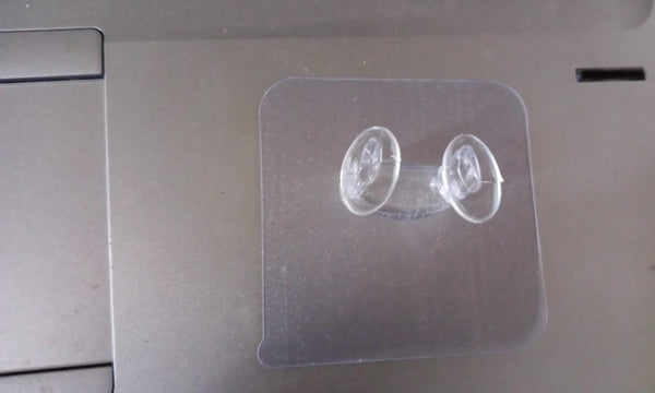 Minimalist transparent self-adhesive wall hook installed on a white wall.