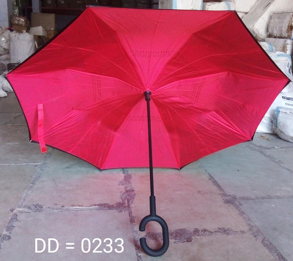 An open, bright red reverse umbrella with a C-shaped handle is displayed on a concrete floor in a warehouse setting.
